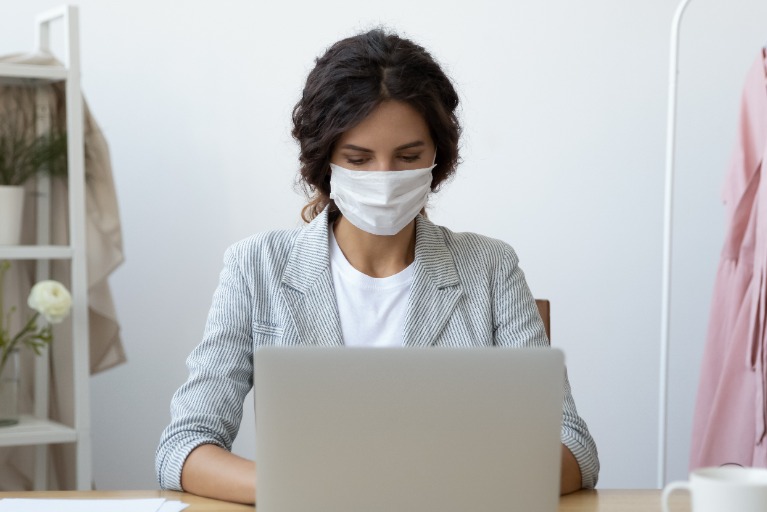 Frau mit Maske am Rechner: Stellenanzeigenschaltung in Krisenzeiten
